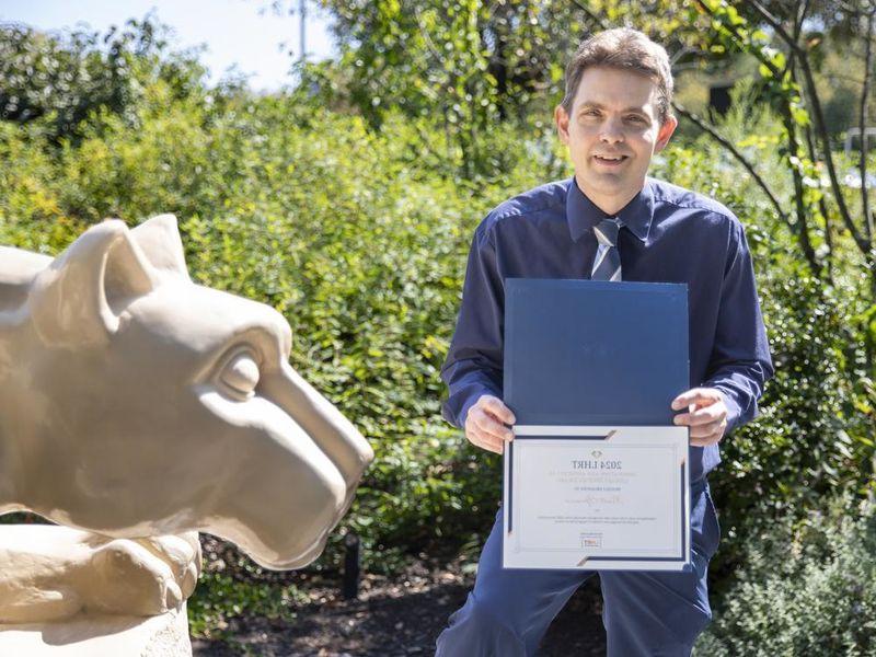 Brett Spencer holding award next to Nittany Lion statue